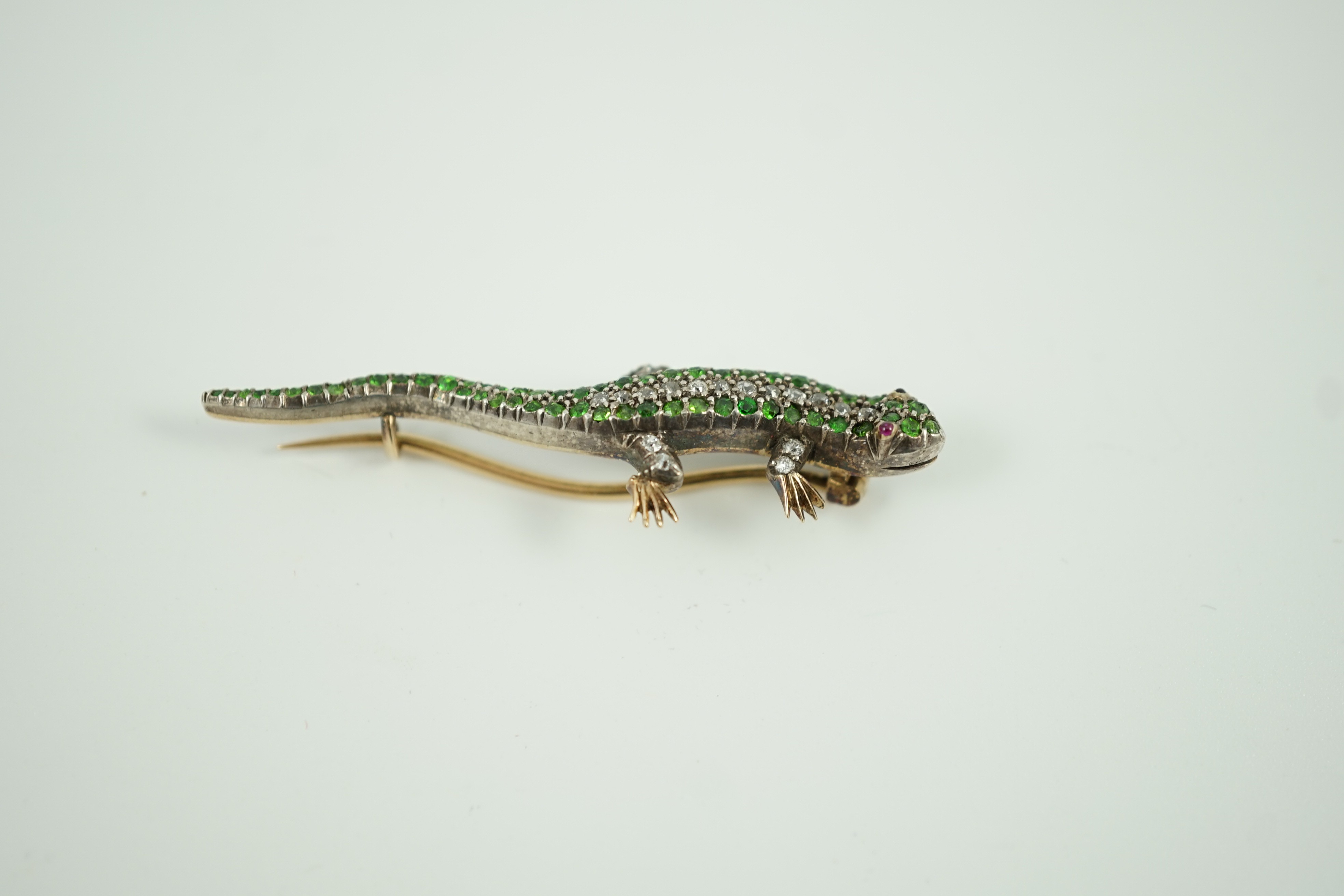 An Edwardian yellow metal, diamond and green garnet set lizard brooch, with red cabochon eyes, 50mm, gross weight 6.2 grams.